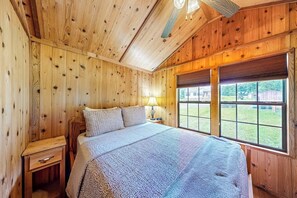 A wooden-paneled room with a bed, a nightstand, a lamp, and a window with blinds. - 1BR houses near lake with firepit, decks, withD, AC (Hector)
