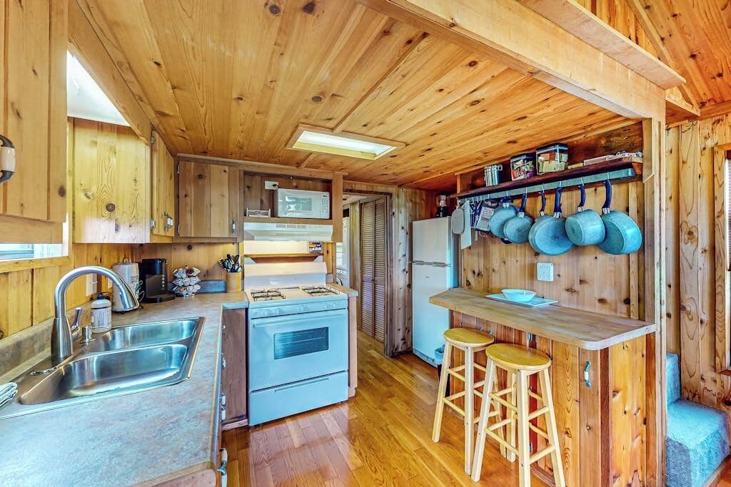 A compact kitchen with wooden walls, a sink, a stove, and a refrigerator.