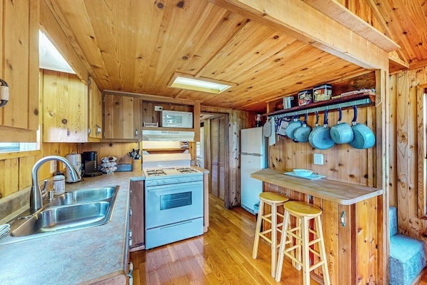 A compact kitchen with wooden walls, a sink, a stove, and a refrigerator.