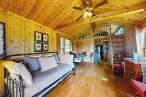 Interior acollidor d'una cabana amb sostre de fusta, un sofà, zona de menjador i una escala.