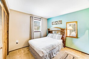 Une chambre à coucher avec un lit, une fenêtre avec des rideaux, un tableau accroché au mur et une petite table avec une lampe.