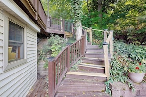 A wooden staircase leading to a deck with a railing, surrounded by greenery and a house. - Willow Bluff | 3 BR lakefront house with private beach & dock (Keuka Park)