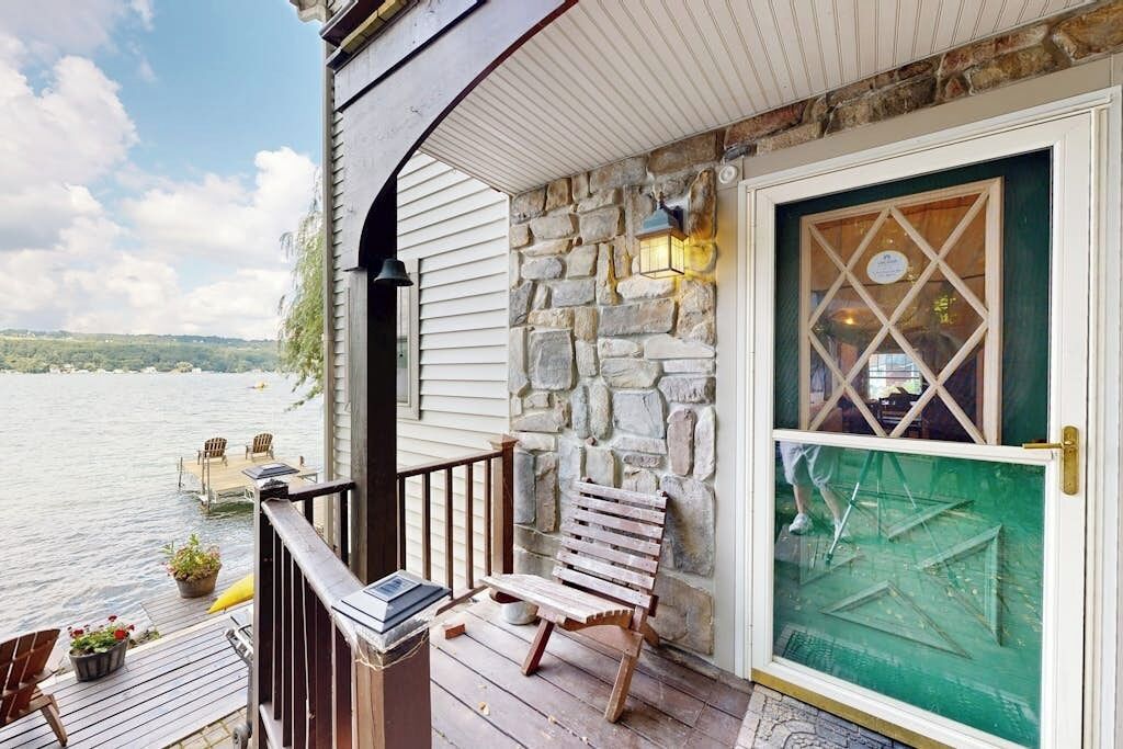 A wooden deck with a stone wall, a bench, and a door with a green glass panel.