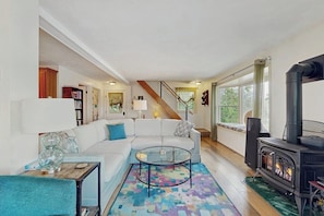 A living room with a white sofa, a glass coffee table, a colorful rug, a fireplace, and a staircase leading to another room. - Willow Bluff | 3 BR lakefront house with private beach & dock (Keuka Park)