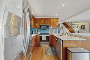 A modern kitchen with stainless steel appliances, wooden cabinets, and a blue tiled backsplash. - Willow Bluff | 3 BR lakefront house with private beach & dock (Keuka Park)