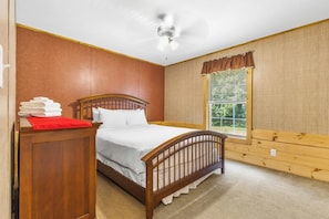 Ein Schlafzimmer mit einem hölzernen Bett, einem Nachttisch, einem Fenster mit Jalousien und einem Deckenventilator.