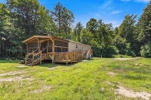 A wooden cabin with a porch and stairs, surrounded by a grassy area and trees. - Private Riverside 3BR house with Guest Cabin (Schroon Lake)