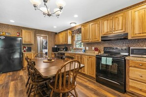 A kitchen with wooden cabinets, a black refrigerator, a stove, and a dining table with chairs. - Private Riverside 3BR house with Guest Cabin (Schroon Lake)