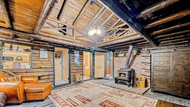 Ein rustikales Blockhaus-Interieur mit Kamin, Ledersofa und einem gemusterten Teppich.