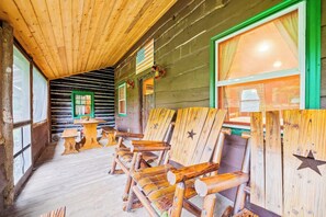 Interior de uma cabana de madeira com móveis rústicos, uma mesa e uma janela com cortinas.