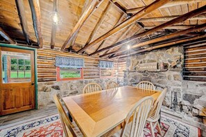 Interior rústico em madeira com parede de pedra, mesa e cadeiras de madeira.