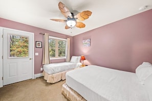 A bedroom with two beds, a ceiling fan, and a window with curtains.