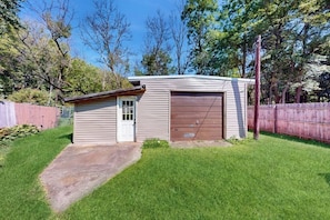 A small, single-story building with a garage, surrounded by a wooden fence and a grassy yard. - 3BR Finger Lakes - Deck - Washer Dryer (Penn Yan)
