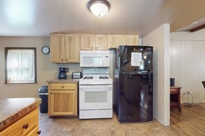 A kitchen with wooden cabinets, a stainless steel refrigerator, a microwave, a stove, and a trash can.