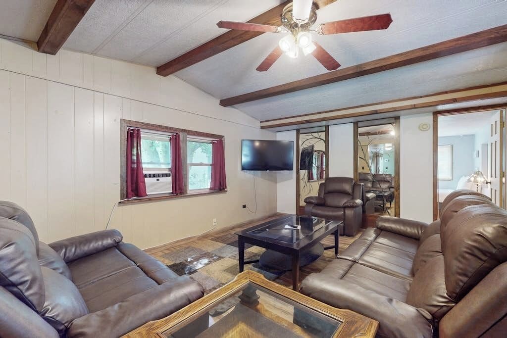 A living room with leather sofas, a glass coffee table, a ceiling fan, and a flat-screen TV.