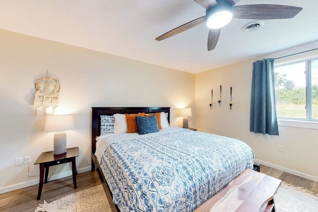 A bedroom with a bed, bedside lamps, a ceiling fan, and a window with curtains.