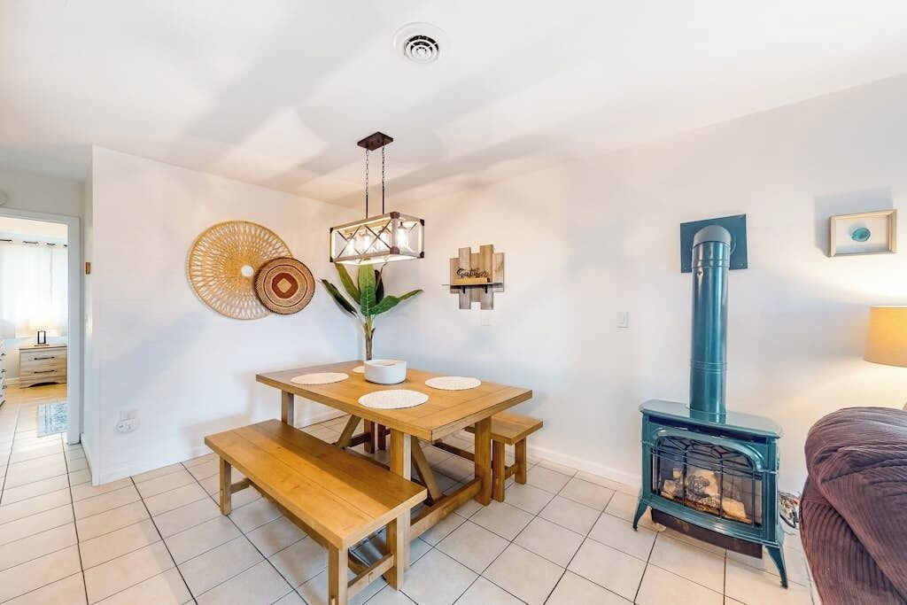 Un salon chaleureux avec une table en bois, des bancs, un poêle à bois bleu et un luminaire suspendu.