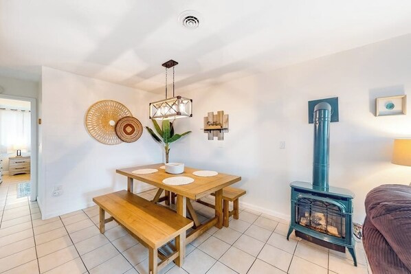 A cozy living room with a wooden table, benches, a blue wood-burning stove, and a hanging light fixture. - Italy Hill Estate | Charming Retreat 2BR Finger Lakes - Hot Tub (Branchport)