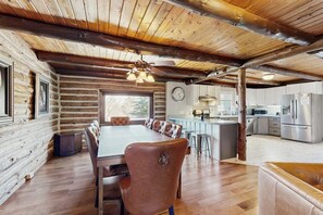Interior d'una cabana de fusta amb zona de menjador, cuina i una finestra gran.