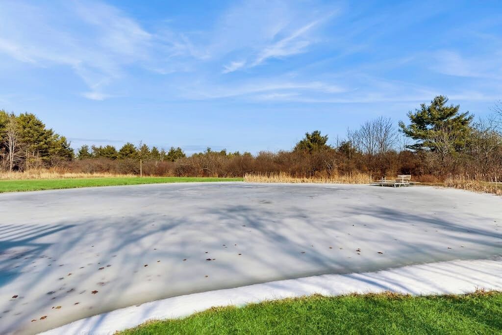 Une patinoire en plein air avec un banc en bois au centre, entourée d’arbres et d’herbe.