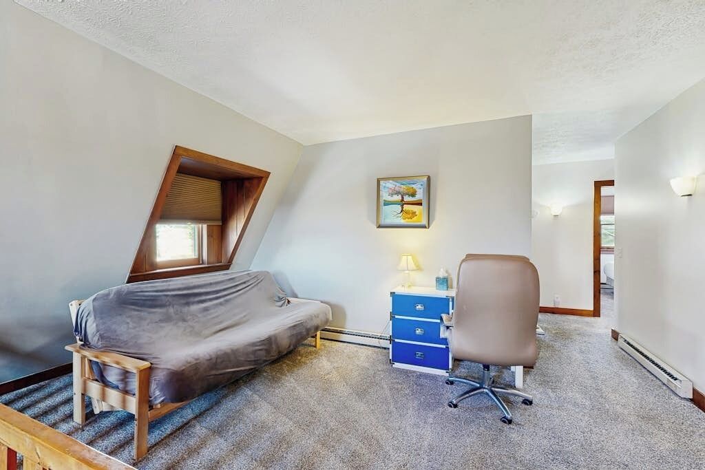A small, compact room with a sloped ceiling, a single bed, a desk with a chair, a small dresser, and a painting on the wall.