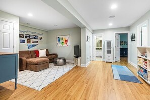 A living room with a sofa, a television, and a rug. There is a hallway leading to other rooms. - Gorgeous 3BR Lakeview Adirondacks Dog Friendly (Hague)