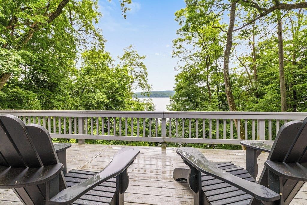 A wooden deck with two Adirondack chairs facing a lake, surrounded by trees.