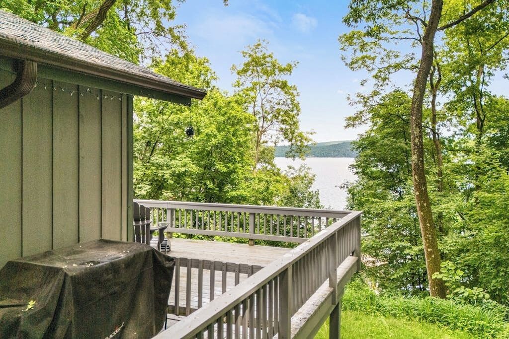 Een houten terras met een leuning, met uitzicht op een meer, omringd door bomen.