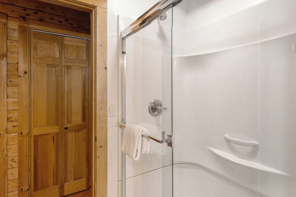 Une porte en bois donnant sur une cabine de douche en verre.