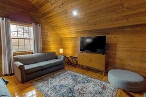 Ein gemütliches Blockhaus-Zimmer mit einer Couch, einem Fernseher, einem kleinen Tisch und einem gemusterten Teppich.