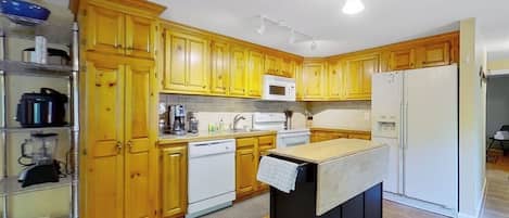 A kitchen with wooden cabinets, a microwave, a refrigerator, and a small island with a sink.