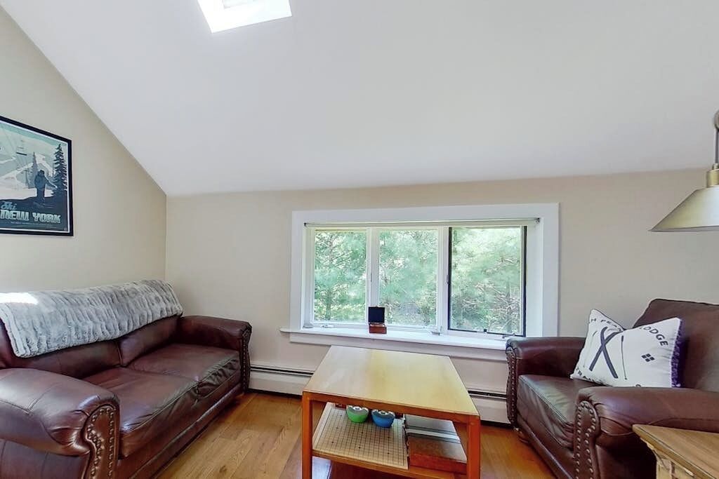 A living room with two leather sofas, a wooden coffee table, and a window with a view of trees.