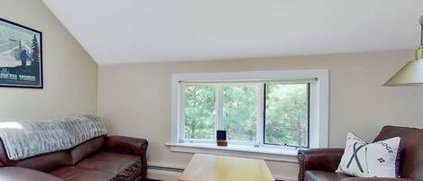 A living room with two leather sofas, a wooden coffee table, and a window with a view of trees.