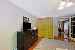 A bedroom with a dark dresser, a television, a wooden wardrobe, and a hallway leading to another room. - 3BR mountain-view house with fireplace (Thurman)