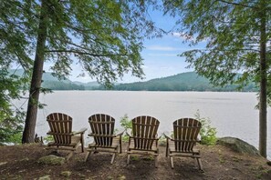 Three Adirondack chairs facing a calm lake with a forested backdrop. - Gorgeous 3BR Lakefront Adirondacks - Dock (Brant Lake)