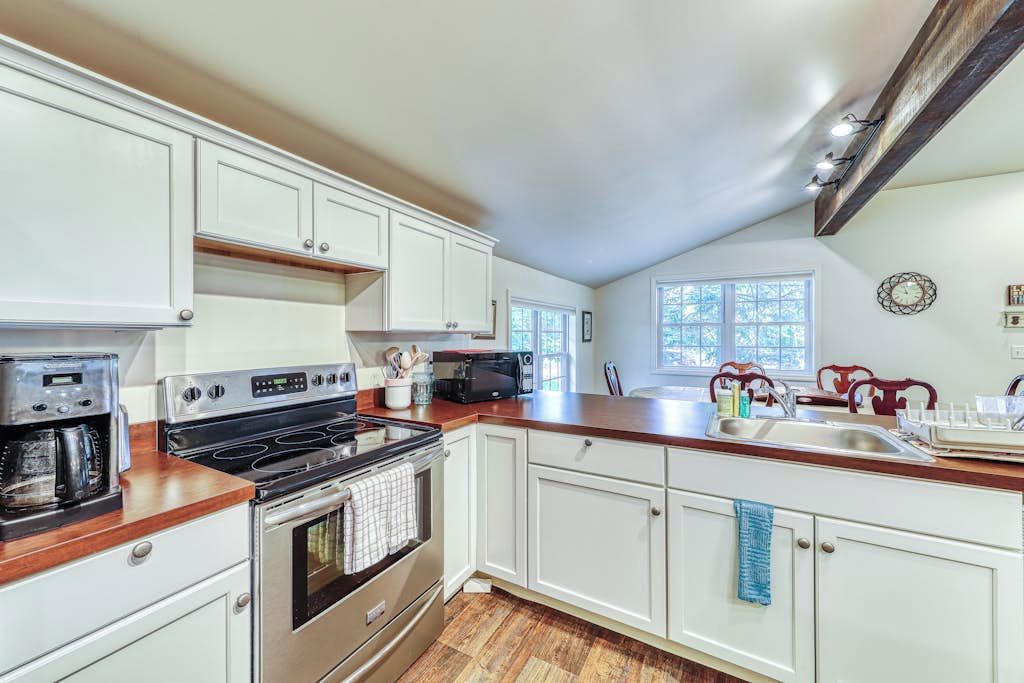A kitchen with white cabinets, a wooden countertop, a stove, and a sink.