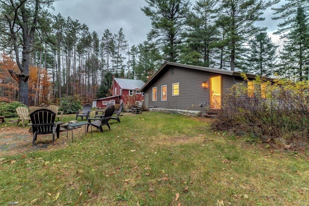 Une cabane avec une façade en bois, une véranda dotée de sièges d’extérieur et un paysage boisé en arrière-plan.