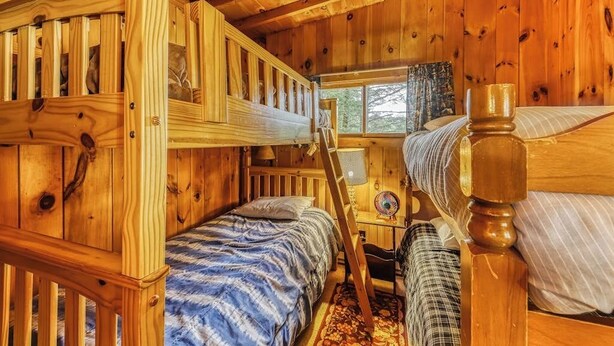 Une cabine équipée d’un lit superposé, d’un bureau avec une lampe et d’une fenêtre donnant sur les arbres.