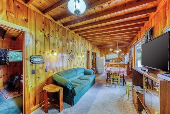 A cozy cabin interior with a wooden ceiling, a sofa, a dining table, and a television.