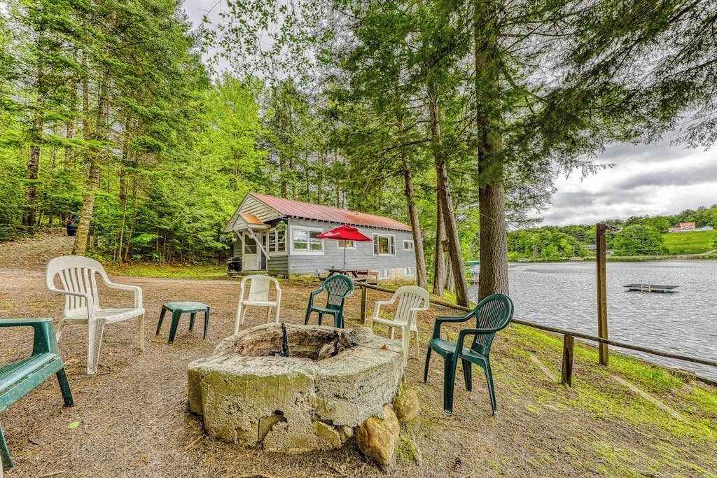 A lakeside cabin with outdoor seating and a fire pit.