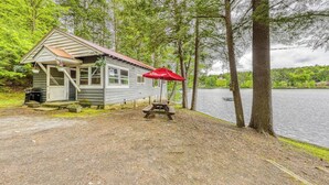 Une cabane avec un parasol rouge, une table de pique-nique et une jetée qui s’avance sur un lac entouré d’arbres.