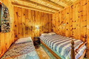A wooden room with two beds, a nightstand, and a wall-mounted lamp.