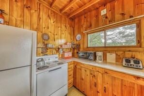 A compact kitchen with wooden walls, a white refrigerator, a stove, a microwave, and a toaster.