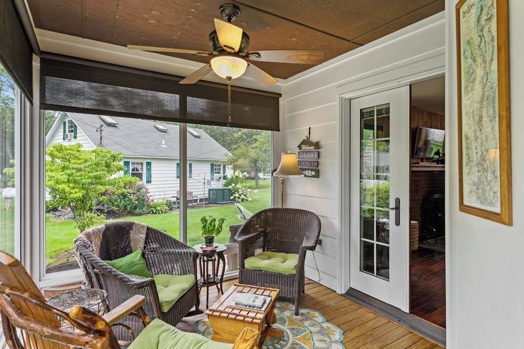 A covered porch with wicker furniture, a ceiling fan, and a view of a house and yard.