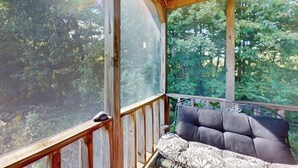 Un terrazza in legno con zona salotto imbottita e ampie finestre che si affacciano su una zona boschiva.