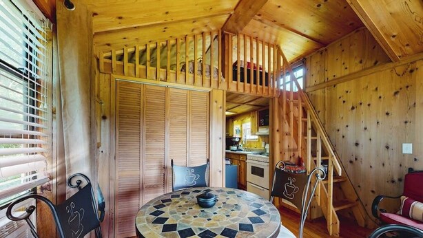 Un interno in legno con un tavolo rotondo, sedie e una scala che conduce a una mansarda.