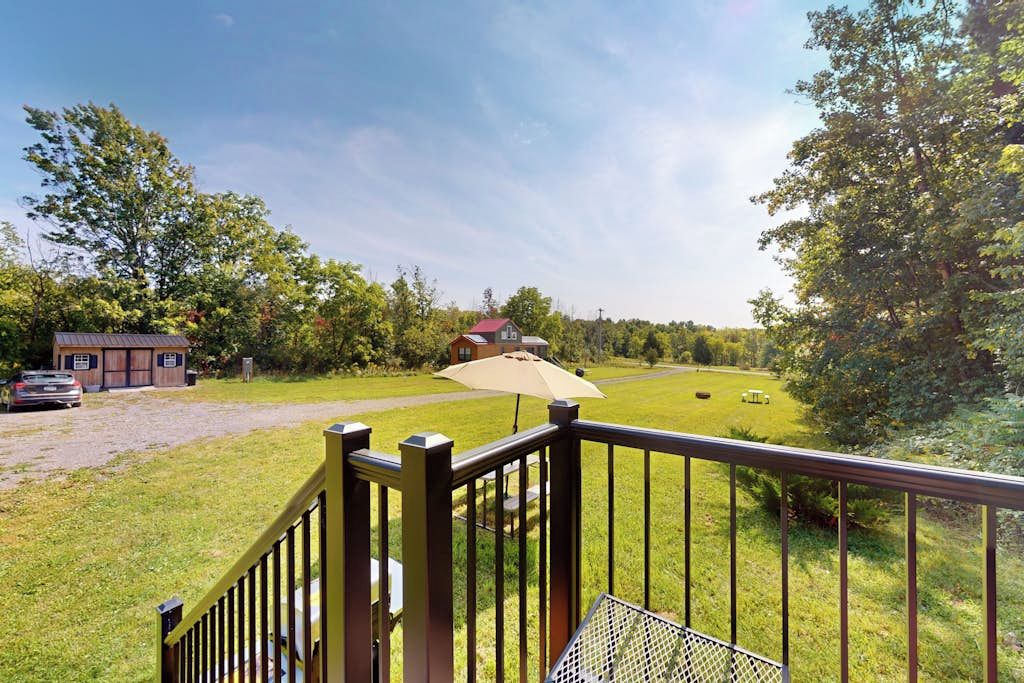 A deck with a metal railing overlooking a grassy area with a building and a car in the background.