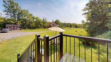 A deck with a metal railing overlooking a grassy area with a building and a car in the background.