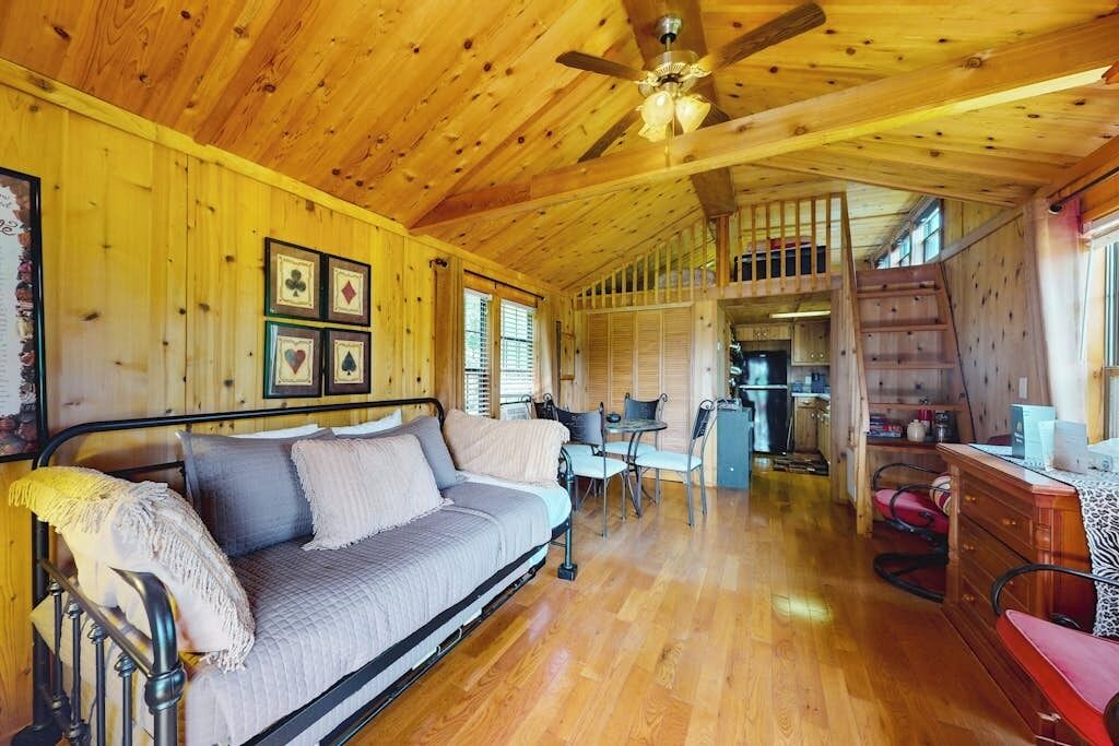 A cozy cabin interior with a wooden ceiling, a sofa, a dining area, and a staircase.