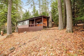 A cabin with a porch, surrounded by trees and a forest floor covered with fallen leaves. - 3BR Lakefront - Fireplace - Dock - Screened Porch (Chestertown)